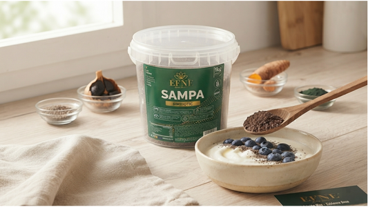 Bote de 1kg de Simbiotic Sampa EFNE LIVING ESSENTIAL sobre encimera de madera en ambiente de cocina natural. Cuchara de madera añade mezcla Sampa a un bol de yogur con arándanos, rodeado de ingredientes como ajo negro y cúrcuma